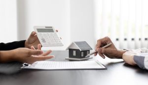 A closeup view of two people, one holding a pen, one holding a calculator reviewing a contract paper over a brown desk