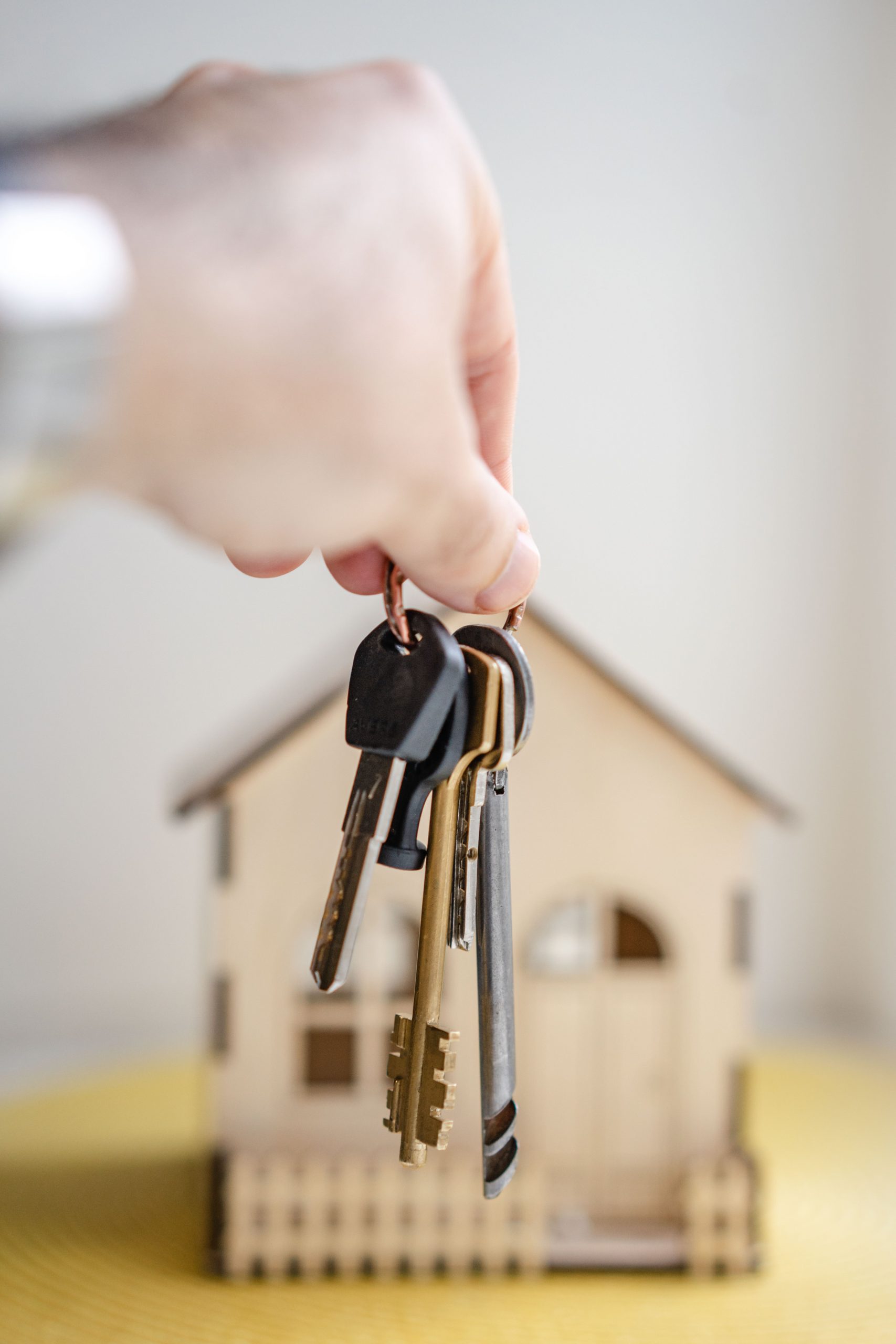 An outsreteched hand dangles keys over a table displaying a miniature wooden house