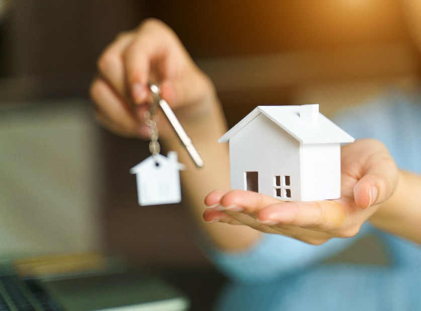 A closeup view of two hands one holding a miniature white house and the other a pair keys